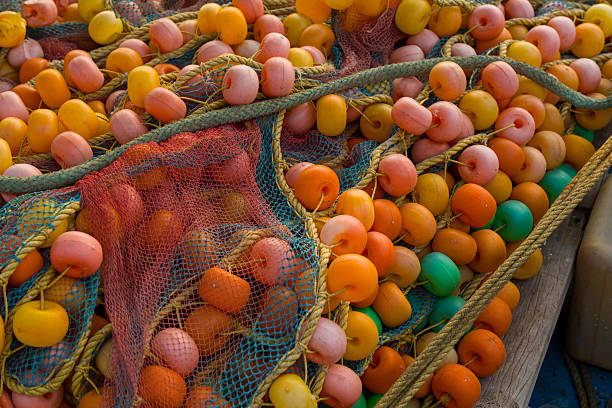Close-up of colorful fishing nets with orange, yellow, green, and pink floats intertwined with sturdy ropes in Kannur, India. The image captures vibrant hues, woven textures, and maritime craftsmanship.