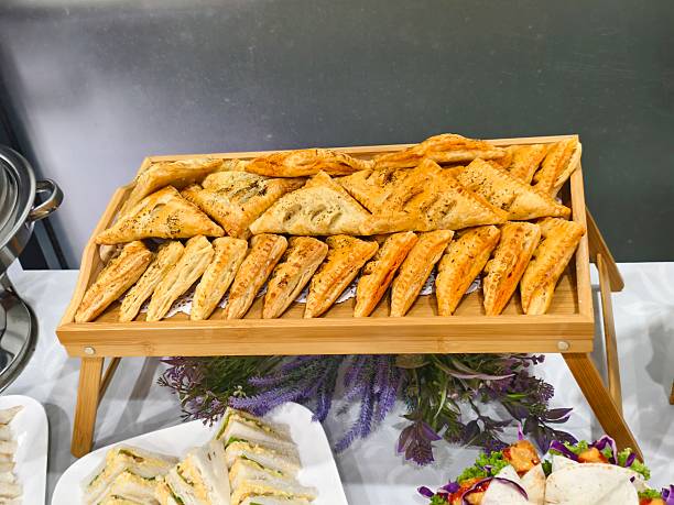 Metal trays with assorted savory pastries and small pizzas are ready to be served at a catered event