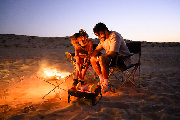 istock Couple camping in desert grilling corn at bonfire during twilight 2255430065