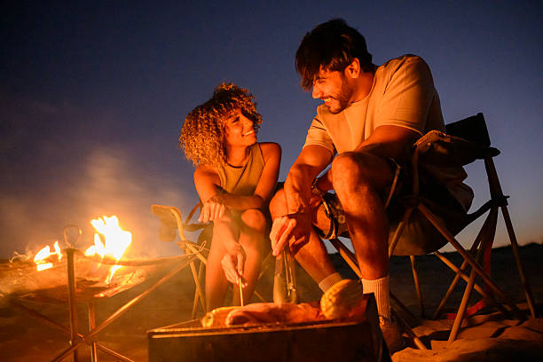 Generation Z tourists sit around camp fire together  under the stars in Al Qudra stargazing area in Al Marmoom Desert Conservation Reserve in Dubai, UAE