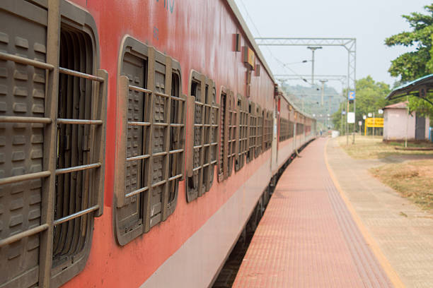 istock Red passenger train standing at an Indian railway station platform with barred windows and empty platform perspective. 2255430634