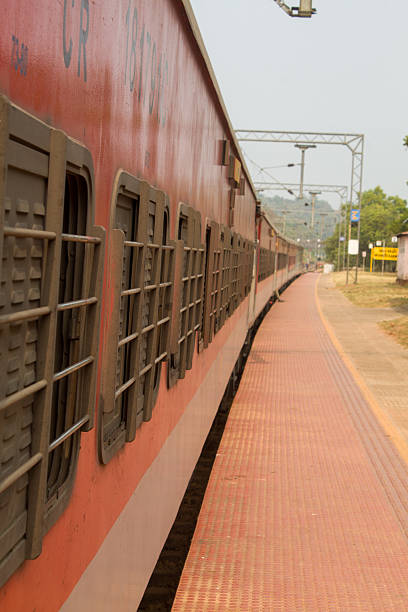 istock Red passenger train standing at an Indian railway station platform with barred windows and empty platform perspective. 2255430660