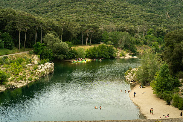 Pont du Gard, France - June 18, 2024: Tourists visit the sand bank and wade in the river below the Roman tiered bridge on a summer day