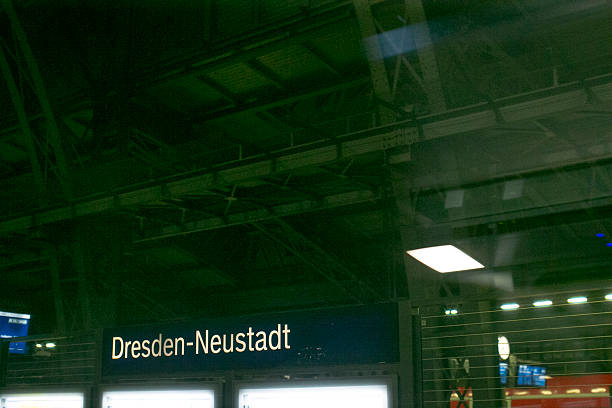 Nighttime DresdenNeustadt train platform, illuminated sign, industrial ceiling and fluorescent lighting create moody urban transit atmosphere empty platform with glowing