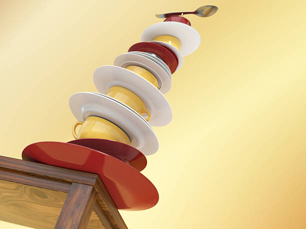 Tall tower of stacked plates and cups sits on a wooden table, showcasing a mix of colors and shapes. The arrangement captures attention with its unique balance and artistic flair. Risk concept.