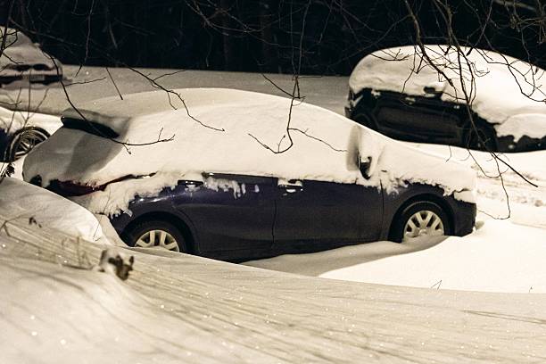 A parked car is completely covered in fresh snow after a heavy winter snowfall during a quiet nighttime scene