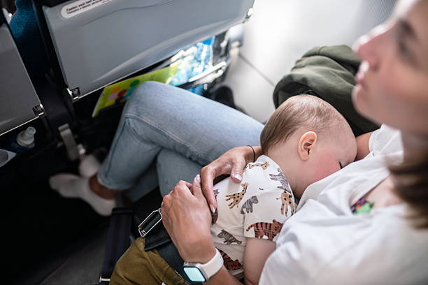 A mother holds a peacefully sleeping baby on her lap in an airplane seat, showcasing warmth, care, and family bonding during travel in a cozy cabin setting.