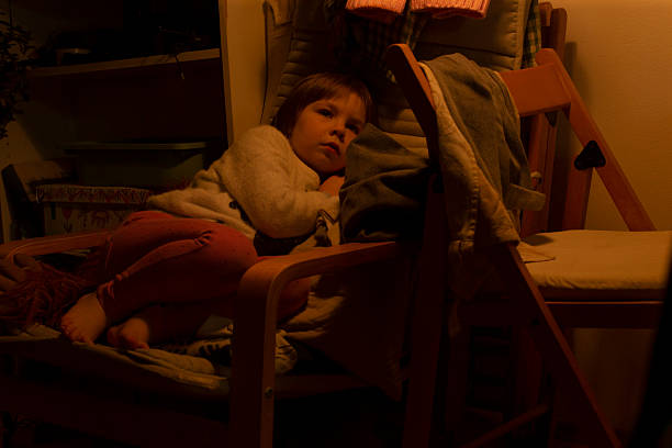 Serene toddler reclining amidst scattered toys, Child peacefully asleep under warm orange glow after playful moment, Young girl rests calmly in quiet comfort as toys are strewn around her