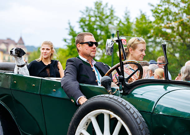 Velden, Austria - August 30, 2025: Vintage car parade showcases a man in sunglasses driving a classic car with two women and a dog enjoying the festive atmosphere