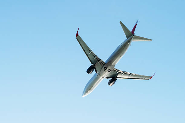 A passenger aircraft flies high in a bright blue sky, photographed from underneath to highlight its wings, engines, and fuselage. The image conveys travel, motion, and modern aviation.