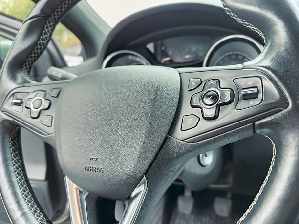 Close up view of a car steering wheel featuring control buttons and leather finish, set against a backdrop of an all-weather dashboard and sleek interior design.