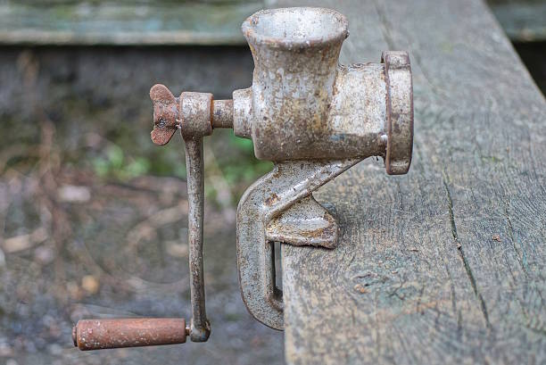 one old gray metal mechanical meat grinder stands on a wooden table in the street
