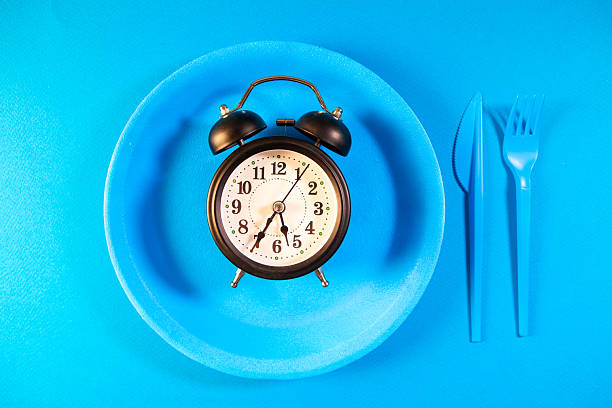 istock Alarm clock on blue plate with fork and knife on blue background 2255450416