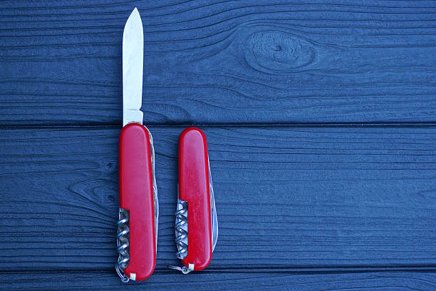 two closed folding knives with red handles lie on a black wooden table