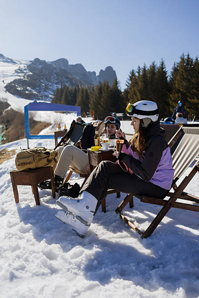 istock Two friends relaxing in ski resort chairs with drinks and snowy mountain backdrop 2255451695