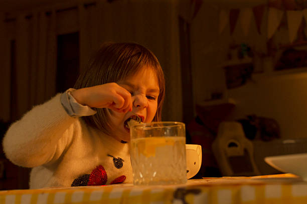 toddler girl stirring snack at table, warm kitchen light, jar of yogurt, lemon drink on checkered cloth, spoon motion,