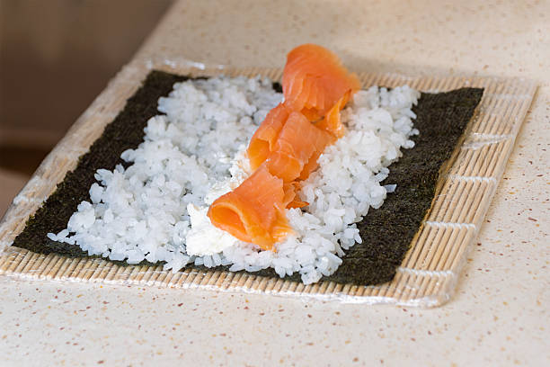 Salmon and rice on nori for sushi preparation on bamboo mat.