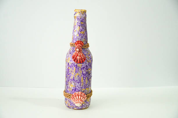 This artistic purple bottle is adorned with gold details, two elegant seashells, and natural rope, perfect as a unique home decoration.