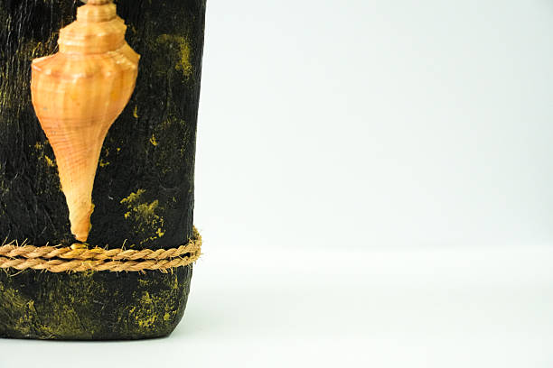 A close-up view highlighting the detailed seashell and rope decoration on the lower part of a dark, textured artisan bottle.