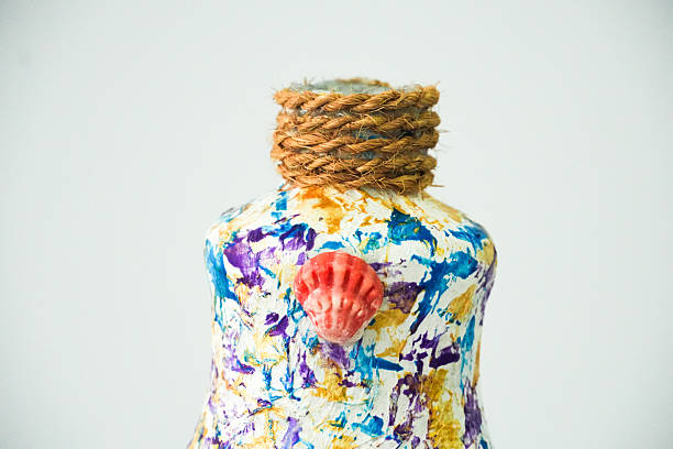 This detailed shot shows the top part of a brightly decorated bottle, featuring a rustic rope-wrapped neck and a small seashell accent.
