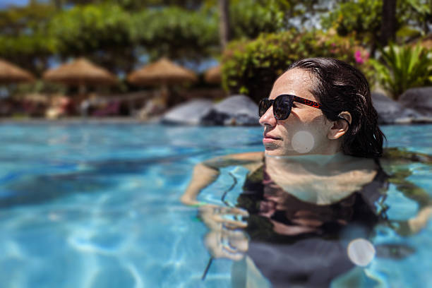 A young Mexican woman wearing sunglasses enjoys a refreshing swim in the resort swimming pool while on vacation in Hawaii.