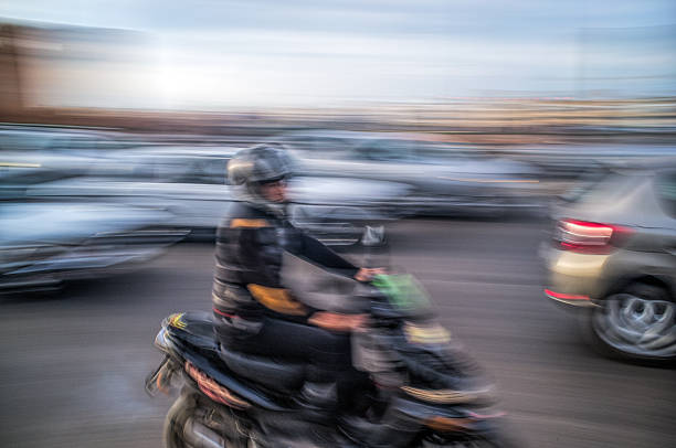 Motorcyclist navigates the busy Avenue Hassan II in Rabat, Morocco. A dynamic panning shot captures the energy of city traffic in motion.