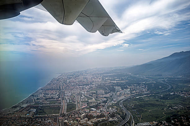 Captures Malaga and the Costa del Sol coastline from an airplane window. Offers a unique perspective of the city and surrounding landscape in daylight.