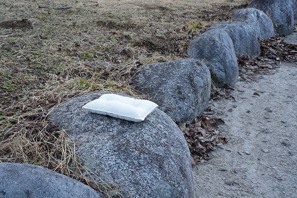 A white pillow is sitting on a rock next to a stone wall. The pillow is placed on a rock that is part of a stone wall. The scene is peaceful and serene