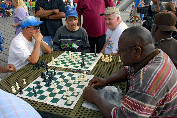 Adult men looks over game pieces on a chess board as they play chess in a downtown detroit michigan park. 01.11.26