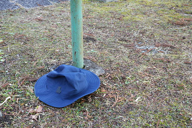 A blue hat is laying on the ground next to a green pole. The hat is upside down and he is abandoned. The scene has a somewhat eerie or abandoned feel to it, as the hat is left alone in the grass