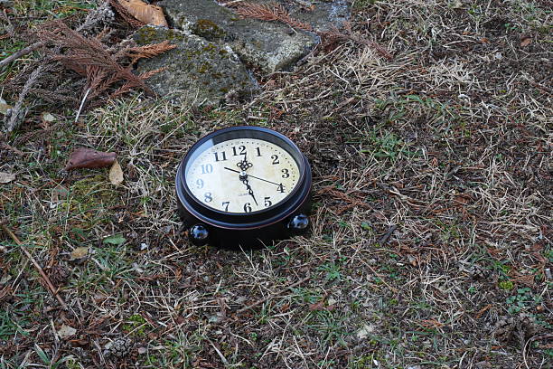 A red clock with the numbers 1 to 12 on it is sitting on the grass. The clock is set to the time of 10:10
