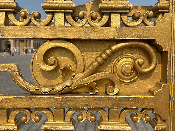 Close-up detail of gilded decorative ironwork on the entrance gates of the Palace of Versailles near Paris, France.