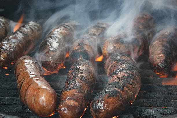 Sausages cook on a charcoal barbecue close up with smoke and flames