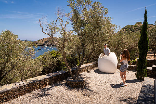 Portlligat, Spain - July 5, 2024: Two tourists pose and photograph each other standing in a giant egg sculpture at the garden of the summer house of the painter Salvador Dali in Portlligat, a small fishing village on the Costa Brava of the Mediterranean Sea, in  Cadaques, Girona, Catalonia