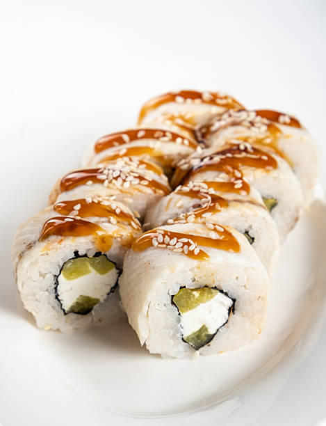 Sushi rolls with cream cheese and pickles, drizzled with sauce and sprinkled with sesame seeds, beautifully arranged on a white plate, showcasing culinary artistry and presentation