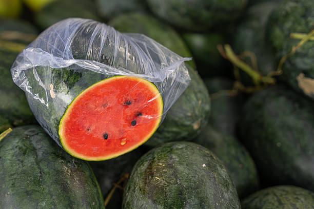 Fresh whole watermelons with a cut slice wrapped in plastic displayed at an Asian local market, highlighting ripe fruit, summer harvest and natural food concept.