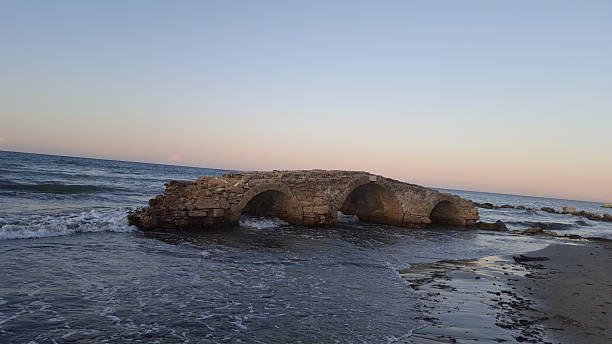 A rugged rock arch frames a stunning coastal landscape beneath a dramatic sky filled with fluffy white clouds, inviting a sense of adventure.