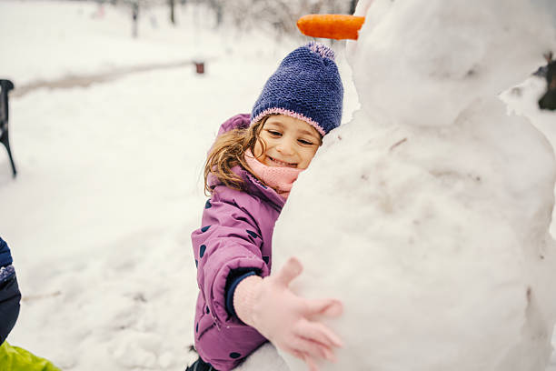 Cheerful preschool age child wearing warm clothes sweetly embracing a snowman, finding delight and experiencing joy during outdoor winter playtime in a snowy park