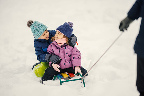 young boy and girl riding together on a sled while going downhill in a snow-covered winter park. Authentic outdoor winter activity showing childhood movement, seasonal recreation, and cold weather lifestyle in a European outdoor setting. Concept of winter activities, outdoor play, and natural leisure.