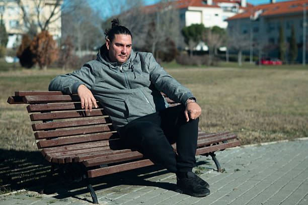 istock Man in hoodie contemplating while relaxing on park bench 2255507066