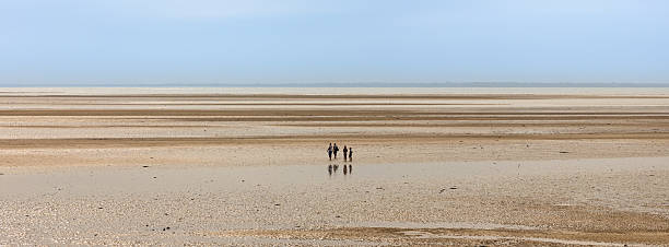 Four people walking on a vast, empty beach of Atlantic ocean in Normandy at low tide, a cloudy sky, minimalism.