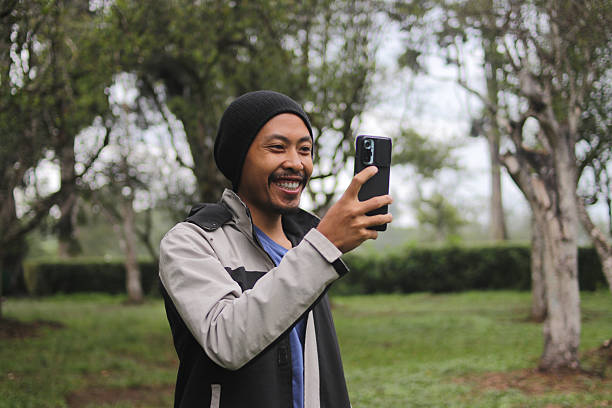 istock Happy Young Indonesian Man Using Phone Outdoors 2255513106