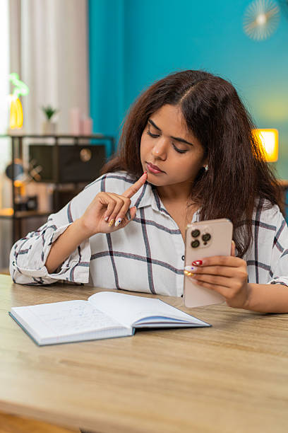 istock Indian woman checks smartphone info cross referencing notebook studying data research indoors focus 2255519748