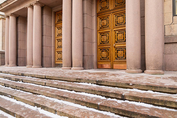 Monumental classical entrance featuring stone columns decorative golden doors and broad steps with traces of snow highlighting historic institutional architecture