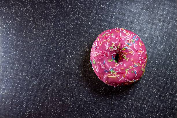 A delightful pink glazed donut with colorful sprinkles on a dark textured surface