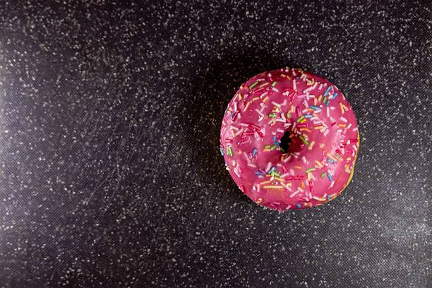 A delightful pink glazed donut with colorful sprinkles on a dark background