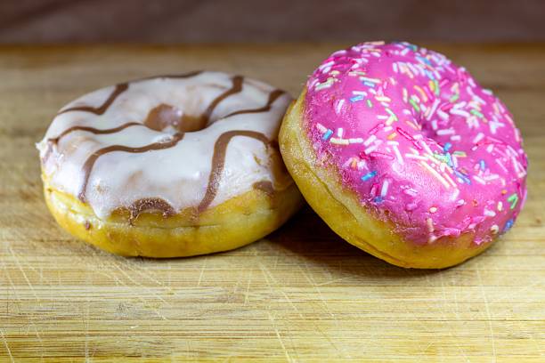 A delightful pair of glazed donuts on a wooden cutting board for dessert