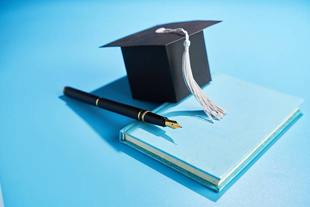 small mortarboard book and pen  against blue background