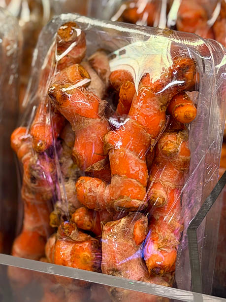 Full frame image of supermarket produce display, prepackaged turmeric roots in plastic tray wrapped in transparent plastic, glass partition screen, focus on foreground, five a day healthy eating concept