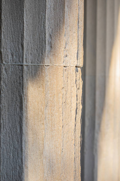 Detail of a weathered architectural column in partial sunlight showing thw texture in the stone.